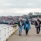 A wide shot of two heterosexual couples wearing warm casual clothing and accessories. They are enjoying a day out in the seaside town of Whitby in February. They are walking along the pier, talking and laughing...Video is also available for this scenario.
1712939087